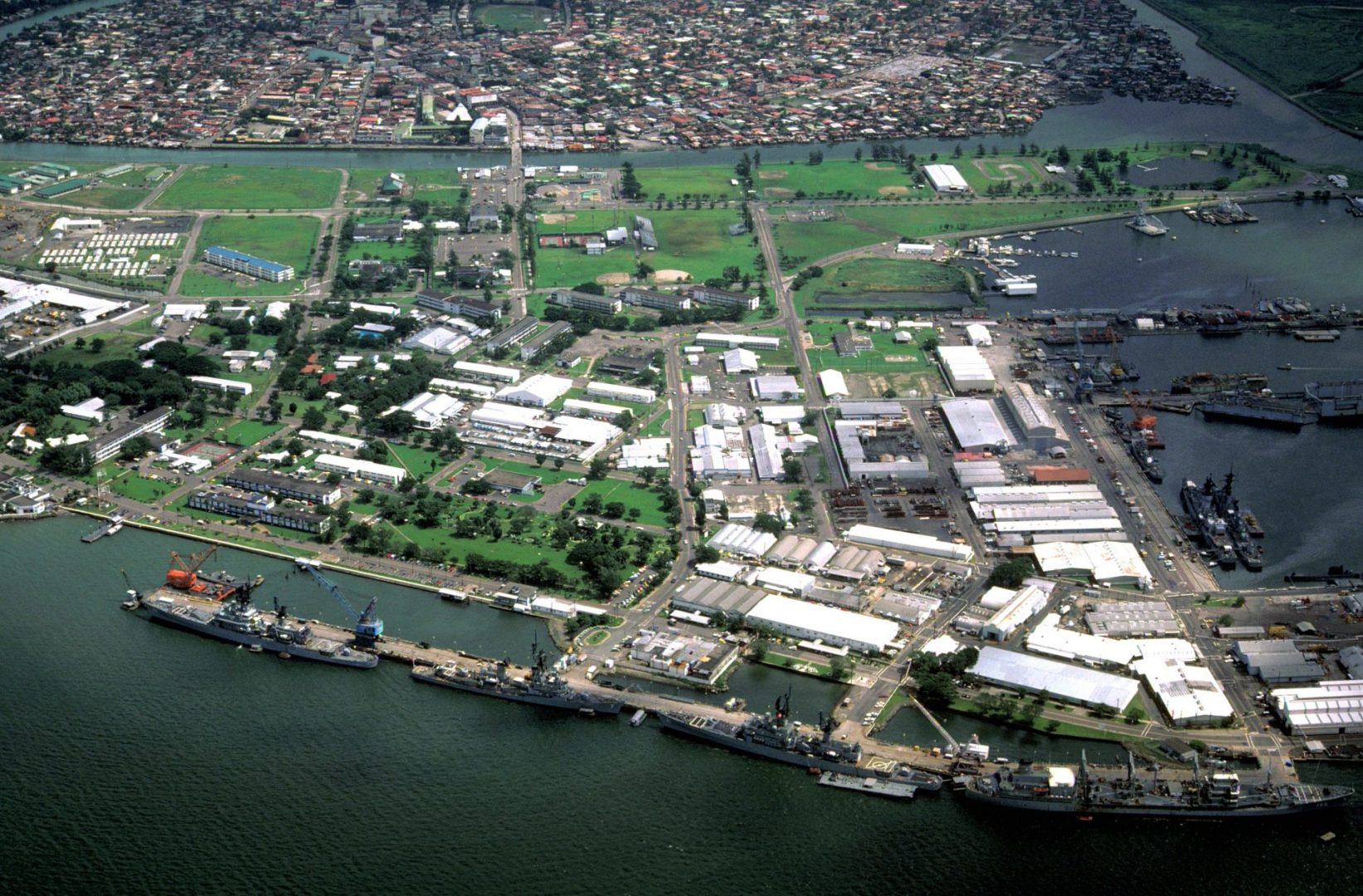 A view of the Naval Base, Subic Bay, with the city of Olongapo in the background. The ships docked at the pier in the foreground are, from right: the oiler USNS HASSAYAMPA (T-AO-145), the guided missile cruiser USS STERETT (CG-31), the guided missile destroyer USS HENRY B. WILSON (DDG-7) and the guided missile cruiser WILLIAM H. STANDLEY (CG-32).